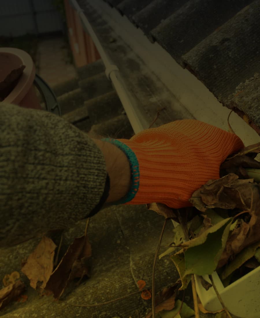 Gloved hand clearing debris from a gutter