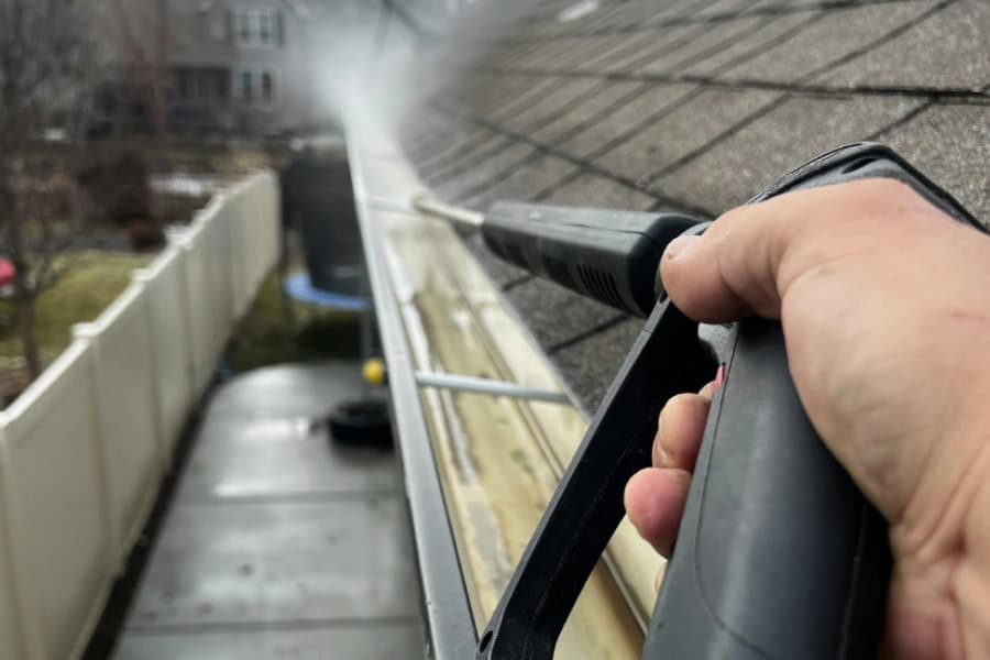Pressure washer rinsing the inside of a roof gutter