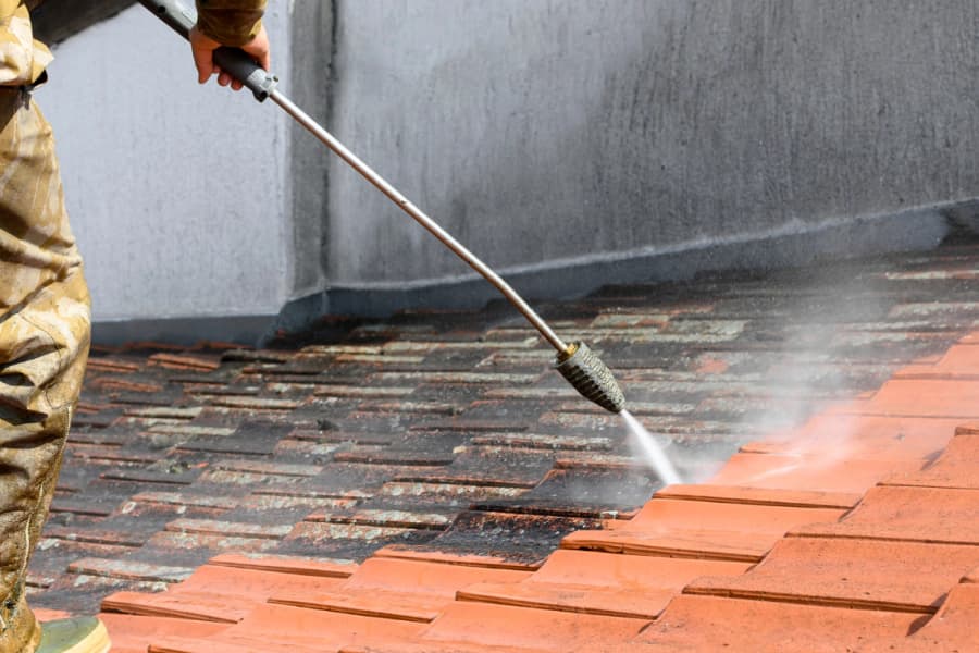 Worker pressure washing a weathered tile roof surface